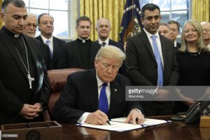 O presidente dos EUA, Donald Trump, assina a “Lei de Socorro e Responsabilidade do Genocídio do Iraque e Síria de 2018” na presença de, entre outros, o arcebispo Bashar Warda de Erbil, no Iraque (à esquerda).